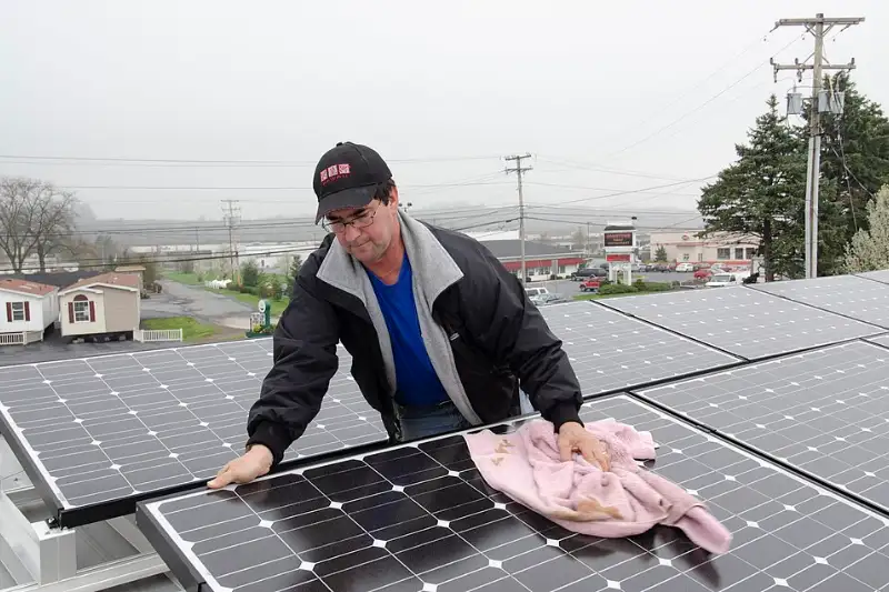 Technician wiping dust off rooftop solar panels during routine cleaning