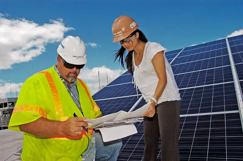 Engineer and project manager reviewing solar installation plans in front of a rooftop array